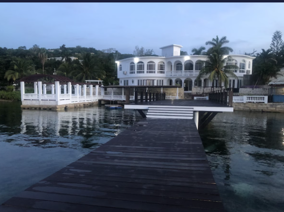Waterfront villa at dusk with arched windows, central balcony and a private dock over calm water